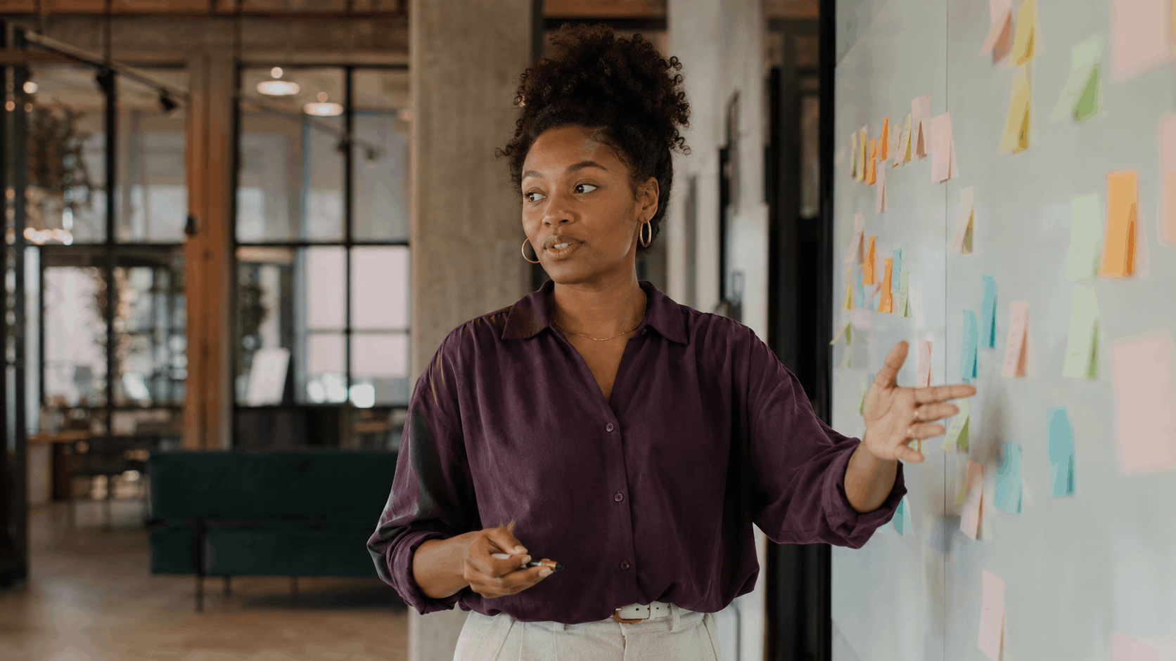 A project manager presenting a plan on a wall of sticky notes in an open-plan office