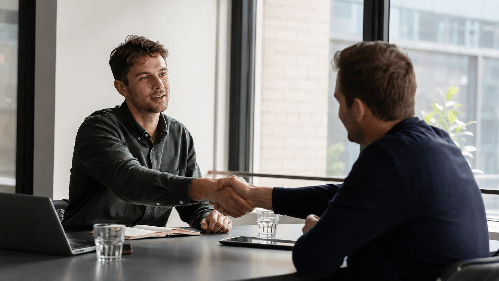 A sales representative shaking hands with a client across a meeting table